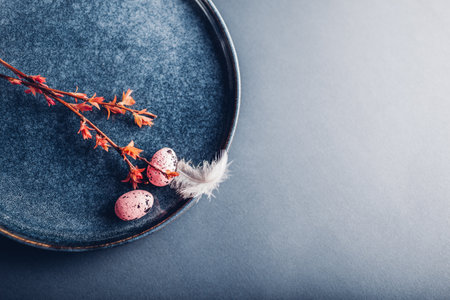 Easter decor. Close up of dishes with eggs, feathers and red spring branches. Ceramic plates on grey background. Space. Holiday mockupの写真素材