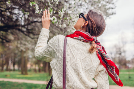 Back view of stylish woman walking wearing red hair scarf and sunglasses in spring park. Retro female fashion. Headscarf for bun hairstyle. Bright accent headscarf.の写真素材