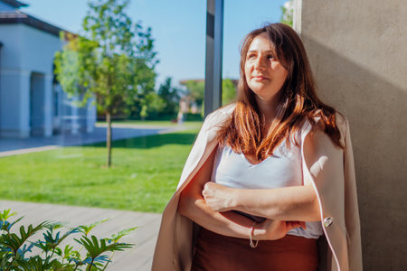 Caucasian businesswoman standing by wall in sunny office. Young serious boss manager having break. Woman wears suitの写真素材