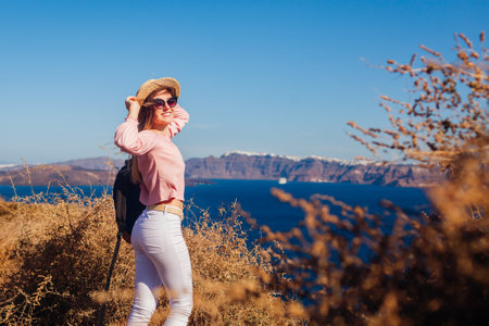 Traveler woman walking on Santorini island, Greece enjoying landscape. Happy girl with backpack enjoys seaside Caldera view. Tourismの写真素材