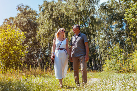 Senior family couple walking outdoors in summer forest. Elderly people holding hands. Romantic date. Man and woman enjoy landscapeの写真素材