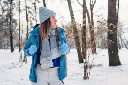 Portrait of young woman putting on blue coat walking in snowy winter park. Warm clothes for cold weather. Sweater seasonの写真素材