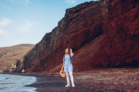 Tourist walking on Red beach on Aegean sea coastline in Akrotiri, Santorini island, Greece. Woman with backpack traveling. Close up of legsの写真素材