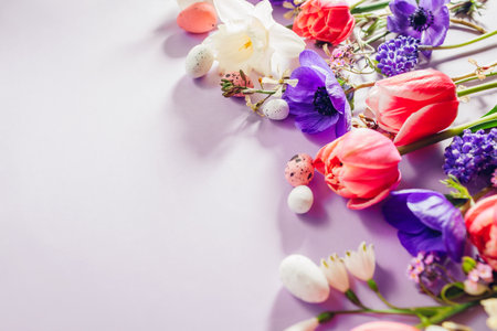 Happy Easter. Easter eggs with spring pink purple flowers flat lay on purple background. Greeting card or banner with blooms. Space. Top viewの写真素材