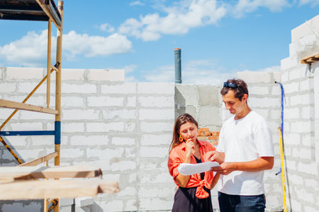 Man architect engineer showing house under construction to woman future homeowner checking blueprint...