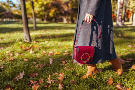 Trendy autumn fashion. Woman wearing grey fall coat, boots, holding burgundy leather purse handbag posing outdoors. Copy spaceの写真素材
