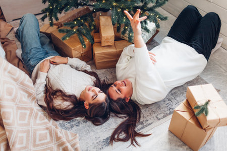 Top view of mother and daughter lying under decorated Christmas tree at home by gift boxes. Holiday family time with kidの写真素材