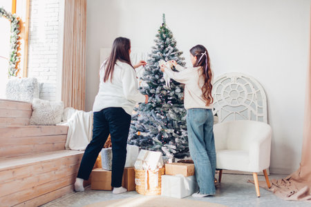 Family decorating Christmas tree with ornaments at home. Mother and daughter enjoying cozy festive atmosphere celebrating holidayの写真素材