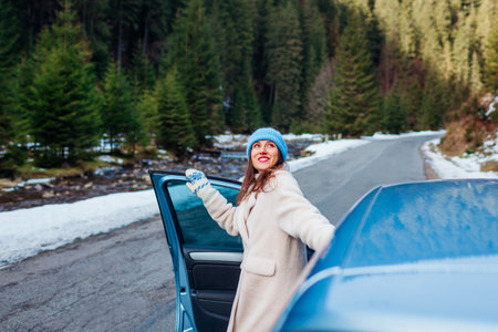 Young woman admiring forest in mountains walking out of car looking at winter landscape. Driver stopped on road among forest. Traveling by auto. Trip to Carpathiansの写真素材