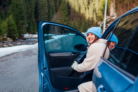 Portrait of woman admiring forest in mountains walking out of car looking at winter landscape. Driver stopped on road enjoying view. Traveling by auto. Trip to Carpathiansの写真素材