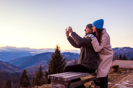 Couple in love taking selfie enjoying landscape of winter Carpathian mountains. Happy man and woman take photo hugging during tripの写真素材