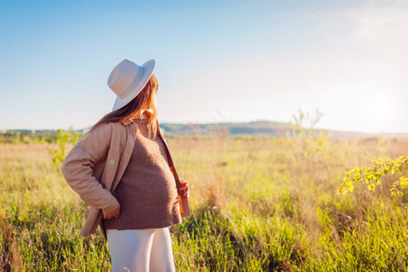 Beautiful pregnant woman walking outdoors at sunset. Future mother wearing stylish clothes and accessories. Motherhoodの写真素材