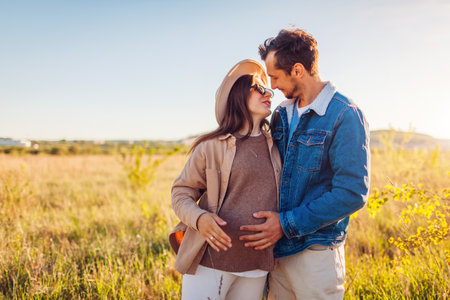 Pregnant family couple walking outdoors. Future parents in love hugging enjoying sunsetの写真素材