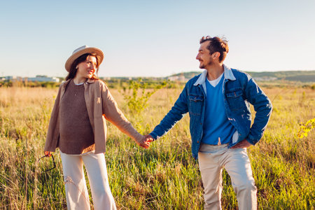 Stylish pregnant family couple walking outdoors. Future parents in love hugging enjoying sunset. Man and woman holding handsの写真素材