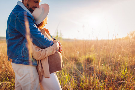 Portrait of pregnant family couple walking outdoors. Future parents in love hugging enjoying sunset. Woman showing her baby bumpの写真素材