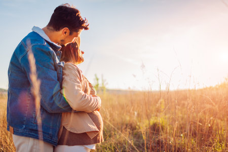 Portrait of pregnant family couple outdoors. Future dad hugging his wife from behind. Woman showing her baby bumpの写真素材