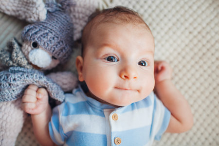 Close up portrait of cute newborn baby lying on couch playing with knitted toy wearing bodysuit....