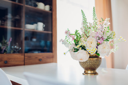 Close up of flower arrangement in brass vase put on dining table. Cozy living room kitchen area. Interior decor with English rosesの写真素材