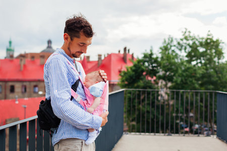 Young father walks with his daughter outdoors while baby girl sleeps in carrier. Babywearing. Child in parent-facing positionの写真素材