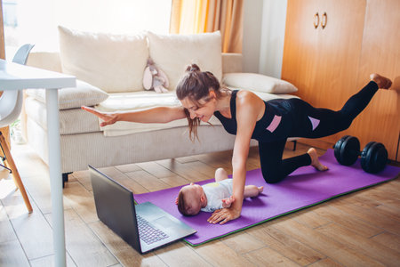 Postpartum recovery training at home. Young mom exercising together with baby girl on yoga mat. Doing sports with infantの写真素材