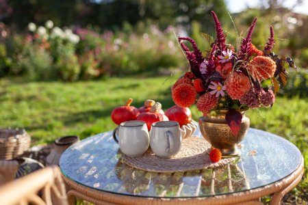 Autumn cozy coffee drinks on backyard in fall garden. Glass table decorated with fall flower bouquet and pumpkins. Breakfast on patioの写真素材