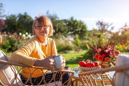 Portrait of senior woman drinking coffee on backyard in fall garden surrounded with autumn decor.の写真素材