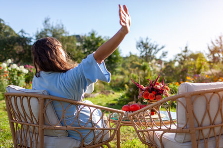 Back view of woman stretching herself wearing pajamas in morning relaxing on terrace in fall garden. Coffee for breakfast outdoorsの写真素材