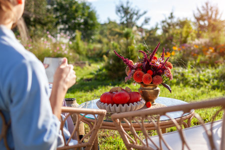 Autumn fall outdoor decor of furniture. Woman having morning coffee relaxing in garden. Table with flower bouquet and pumpkins.の写真素材