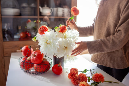 Woman makes bouquet in vase full of dahlia flowers on table with pumpkins. Interior and home decor. Autumn floral arrangementの写真素材