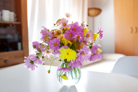 Close up of flower arrangement made of pink cosmos and yellow dahlias. Bouquet put on dining table in living roomの写真素材