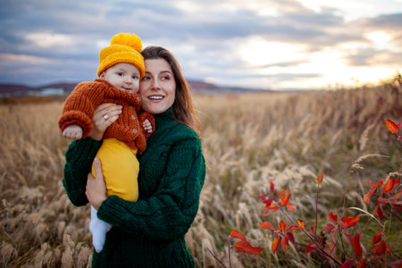 Portrait of young mother holding baby girl walking outdoors on fall meadow. Family wearing warm knitted clothes. Spaceの写真素材