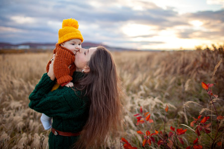 Happy young mother kissing baby girl outdoors on fall meadow. Woman hugging infant. Family wearing warm clothes. Spaceの写真素材