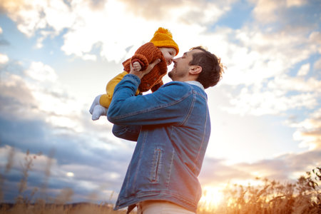 Young father rising baby girl up walking outdoors. Family wearing warm fall clothes. Family having funの写真素材
