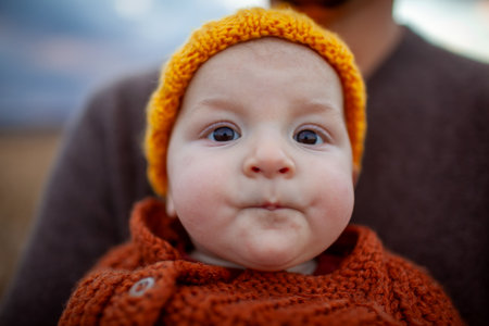 Close up portrait of little baby girl on fathers hands. Infant child wearing warm fall yellow hat and brown sweater.の写真素材