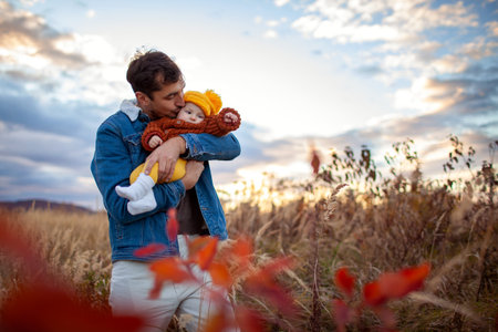 Happy man kissing his little baby girl walking outdoors. Father holding infant daughter wearing fall brown sweater and yellow hatの写真素材