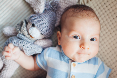 Close up portrait of cute newborn baby lying on couch playing with knitted toy wearing bodysuit. Infant smiling. Top viewの写真素材