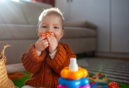 Happy baby girl playing with sensory ball. Child chewing educational toy sitting on floor at home. Infant learns and has funの写真素材