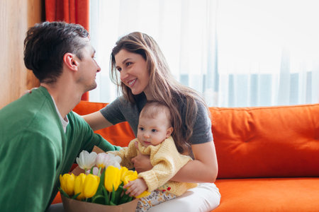 Happy Mothers day. Husband surprising his wife with bouquet of flowers at home. Woman holding...