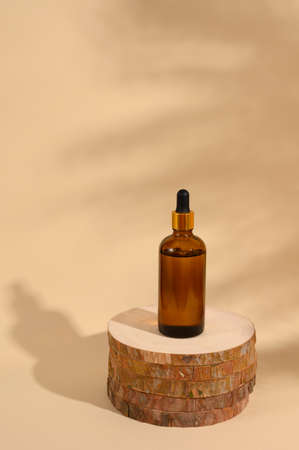 Round wooden podium with glass bottle on beige background. Monochrome creative composition with shadow. Front view. Copy space.の写真素材