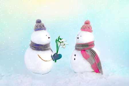 Snowmen in love on a beautiful background in pink and blue colors. Boy giving snowdrop flowers to girl. Spring, love concept. Copy space.の写真素材