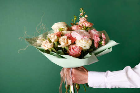 Man holding and giving a beautiful bouquet with flowers to woman on green background. Front view....