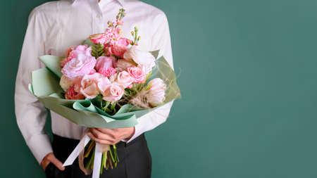 Man holding and giving a beautiful bouquet with flowers to woman on green background. Front view. Valentines, womens, mothers day, love concept. 8th of march. 14th of february.の写真素材