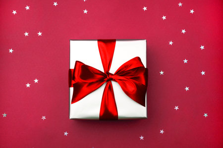 Gift box with bow on red color background with sparkles. Christmas,New Year, Valentine's day, Birthday concept.の写真素材
