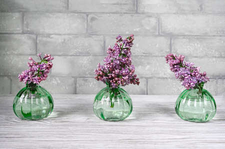 Lilac flowers in vases on a table against grey brick wall. Front view. Spring concept.の写真素材
