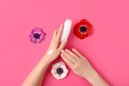 Woman applyiing cosmetic cream on her hands on pink background with flower and leaves. Home spa, beauty and treatment concept. Flat lay, top view.の写真素材