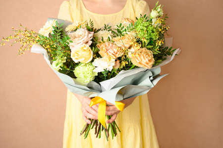 Woman in yellow dress holding a beautiful bouquet with flowers on beige background. Front view. Valentines, womens, mothers day. Spring, summer concept.の写真素材