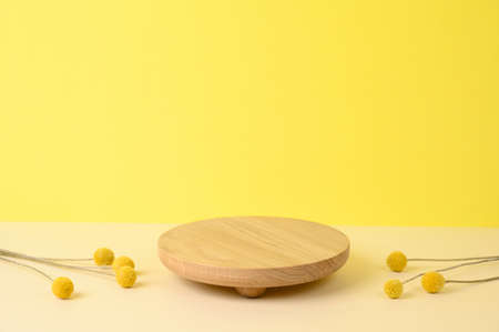 Round wooden podium on beige and yellow background with dried flowers for product presentation. Front view. Copy space.の写真素材
