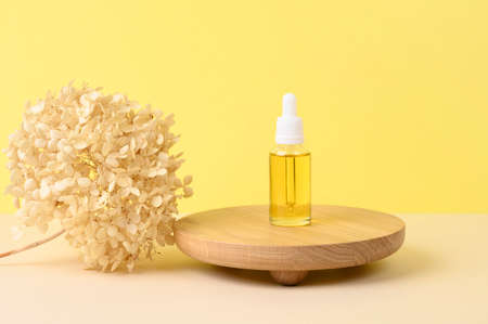 Round wooden podium with cosmetic bottle, dried flower on beige and yellow background for product presentation. Front view. Copy space.の写真素材