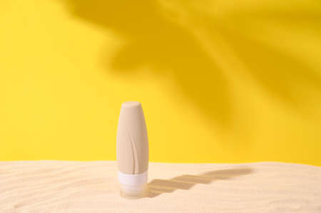 Cosmetic jar on sandy podium against summer yellow background with shadow of leaves. Concept of...