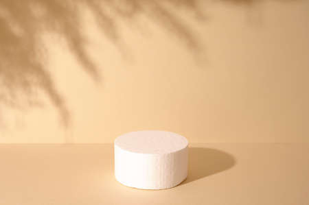 White round podium for cosmetic product against beige background and shadow of leaves. Front view.の写真素材